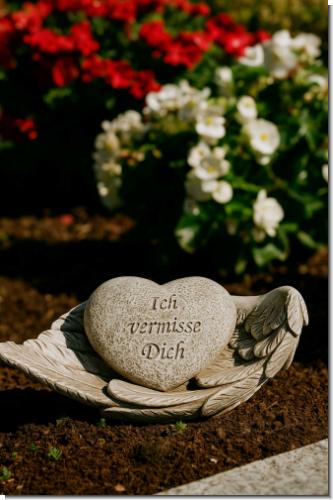 Herzförmige Gedenkfigur „Ich vermisse Dich“ auf Engelsflügeln. Wetterfestes Polyresin in Steinoptik – liebevoller Grabschmuck & Erinnerung.