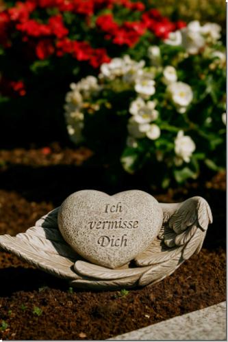Herzförmige Gedenkfigur „Ich vermisse Dich“ auf Engelsflügeln. Wetterfestes Polyresin in Steinoptik – liebevoller Grabschmuck & Erinnerung.